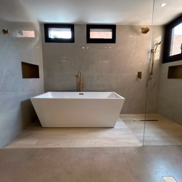 Remodelación de baño moderno con tina independiente, revestimientos de alta gama y mampara de cristal templado
